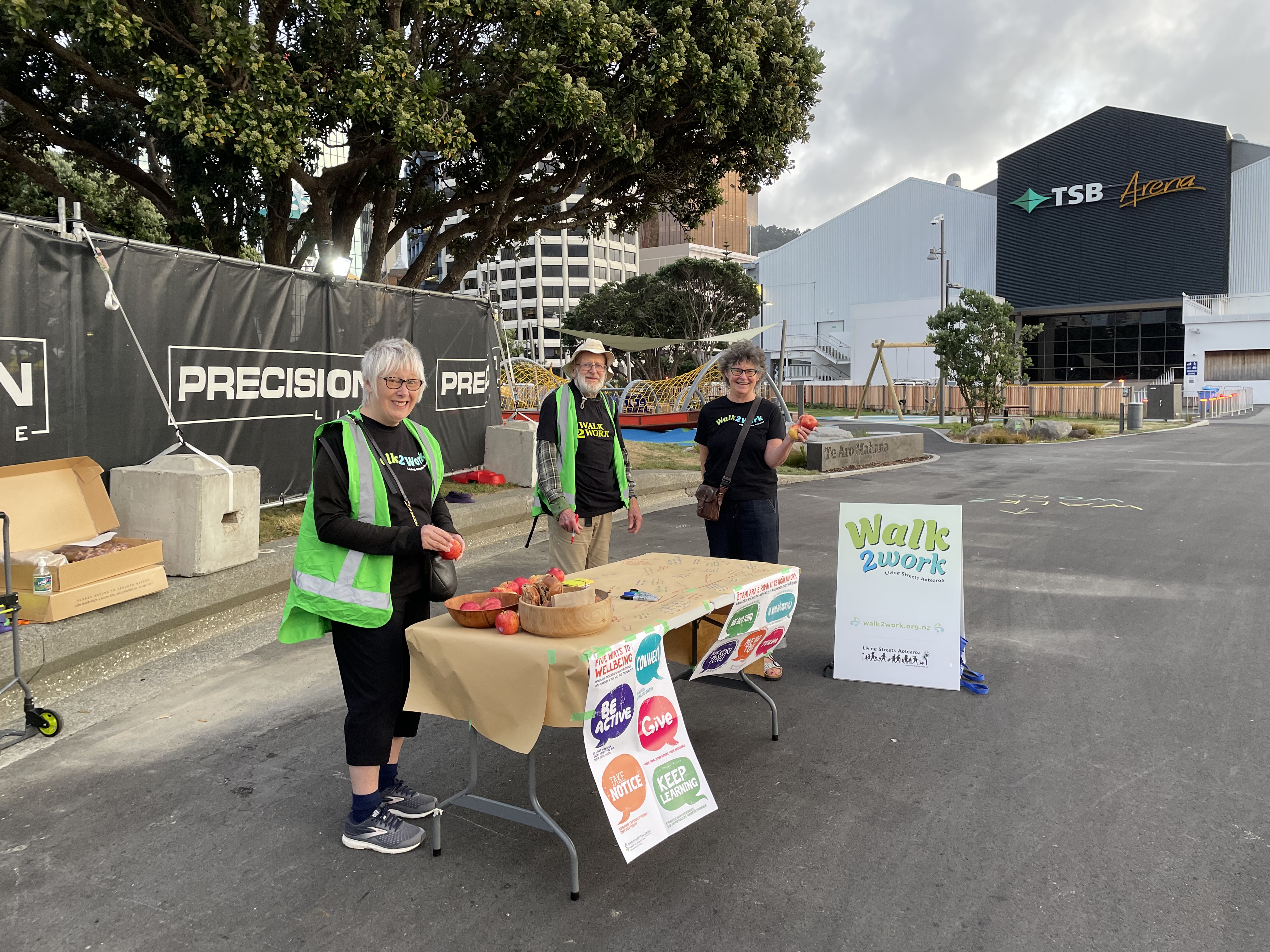 Three people from Living Streets Aotearoa with a table with signage for Walk2Work Day. 