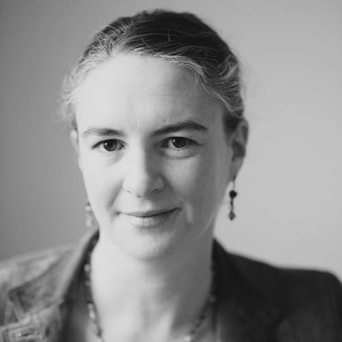 A black and white image of Antonia Malchik with hair back, wearing a jacket and beaded earrings and necklace