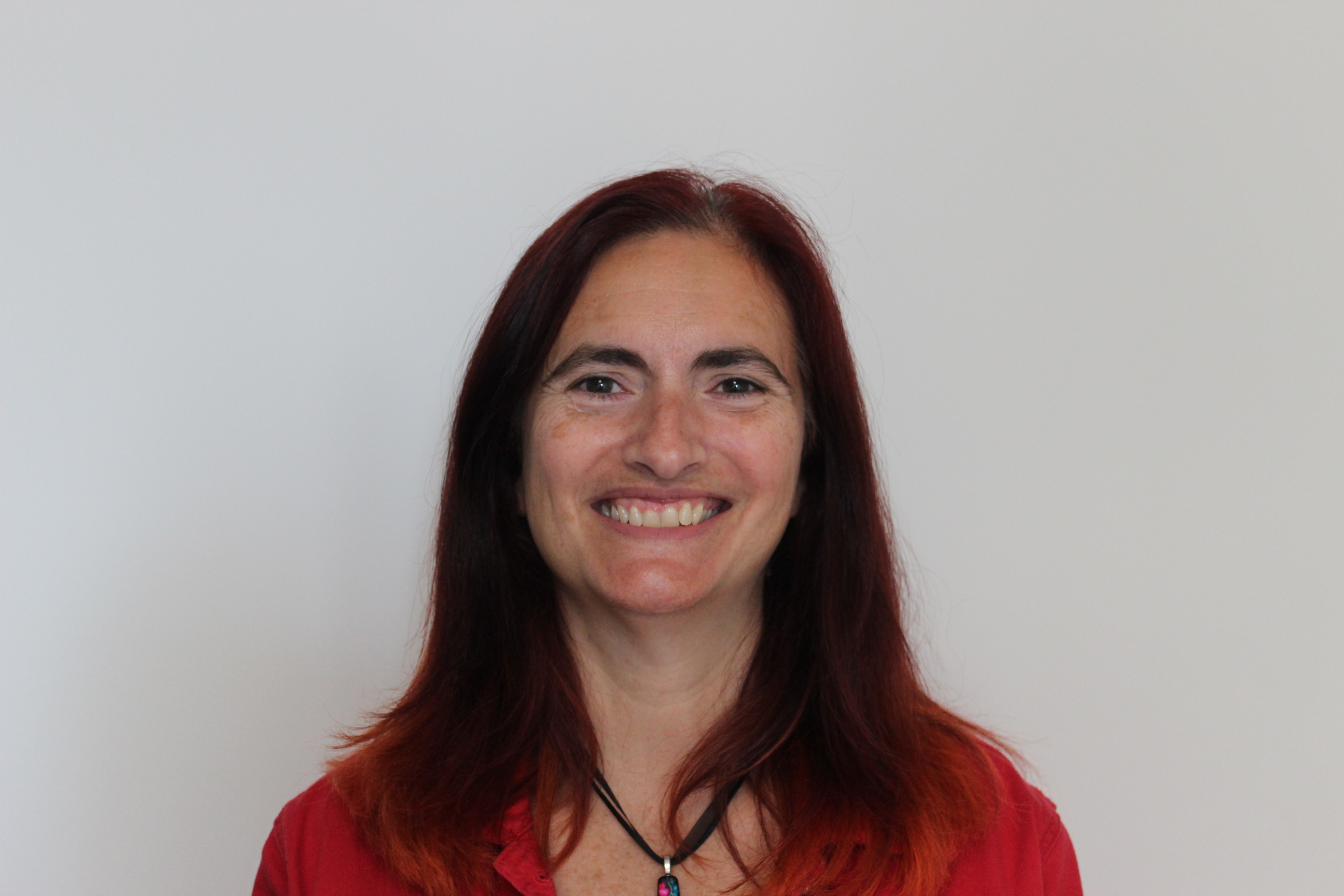 An image of Patrícia Vasconcelos with brown eyes, long dark hair, a red shirt, and necklace. 
