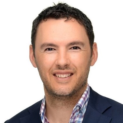 A headshot of Peter McGlashan with short brown hair, brown eyes, and a beard, wearing a checked button down and jacket