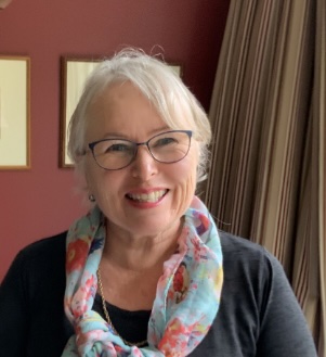 An image of Rosie Woods wearing a black shirt and colourful scarf, with a white bob and glasses