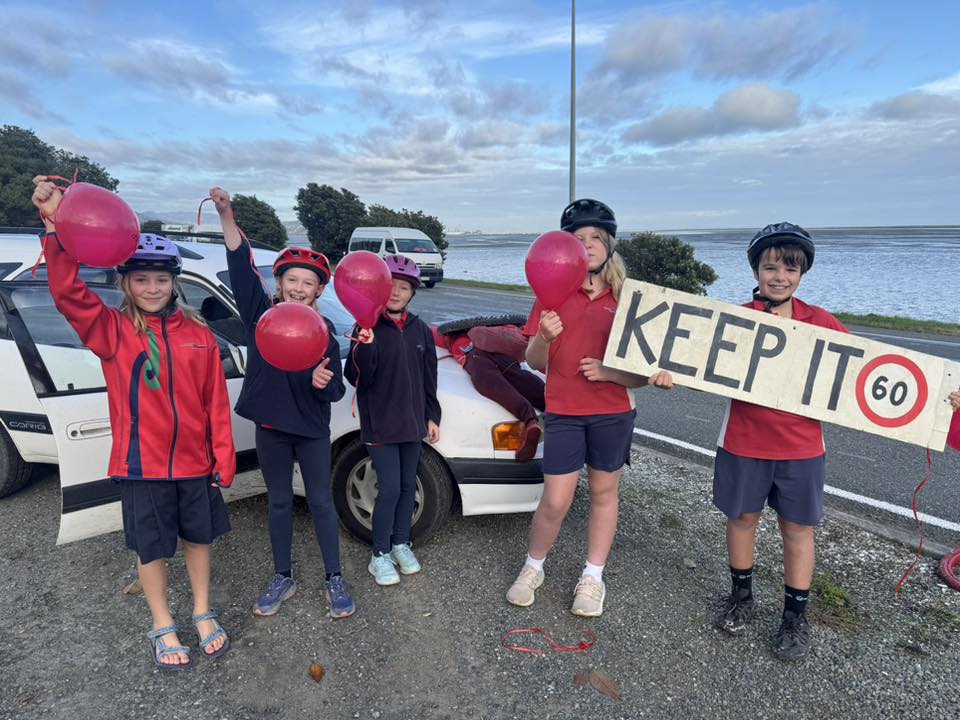 Children holding balloons and a sign saying keep it 60 next to a staged crash