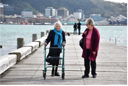 Muriel with walking frame and walking companion by her side on a wharf
